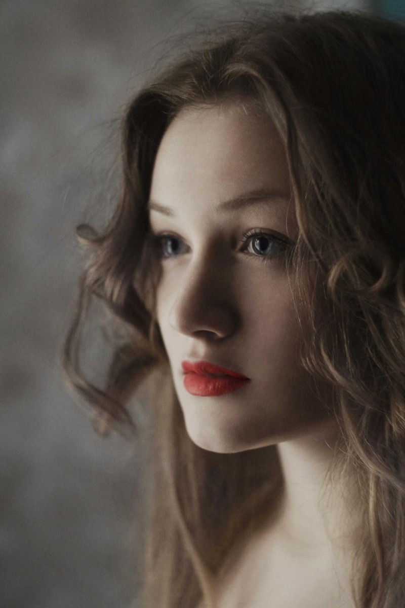Studio portrait of a young woman with wavy brown hair and red lips against a dark grey background